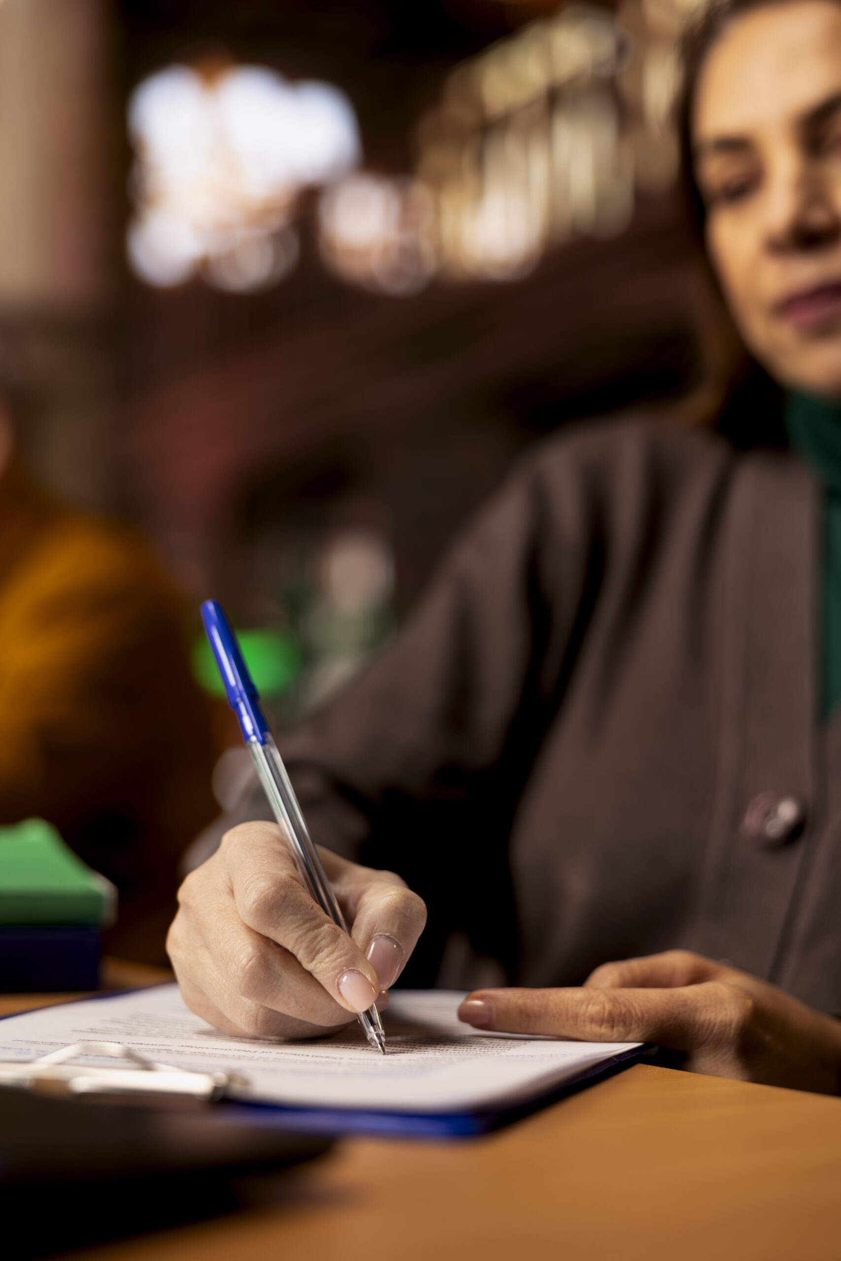 Adult learner transcribes information during a lecture in a university library, surrounded by academic textbooks and archived documents. Higher education personal goals on campus. Close up.